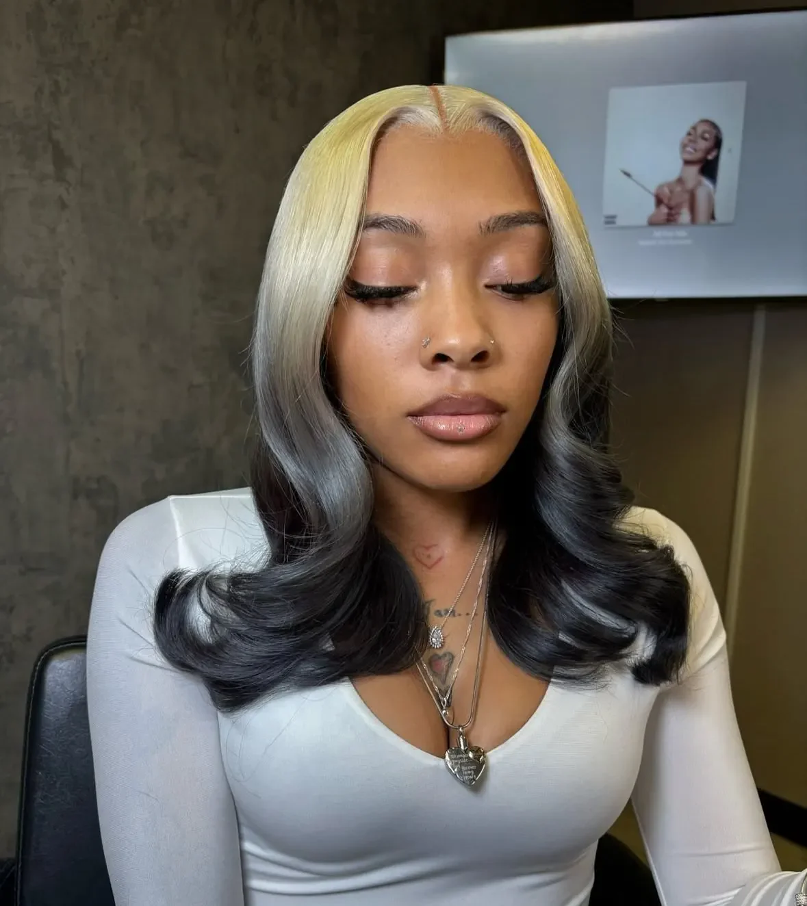 Woman with medium black body-wave hair and blonde color placed near the front roots.