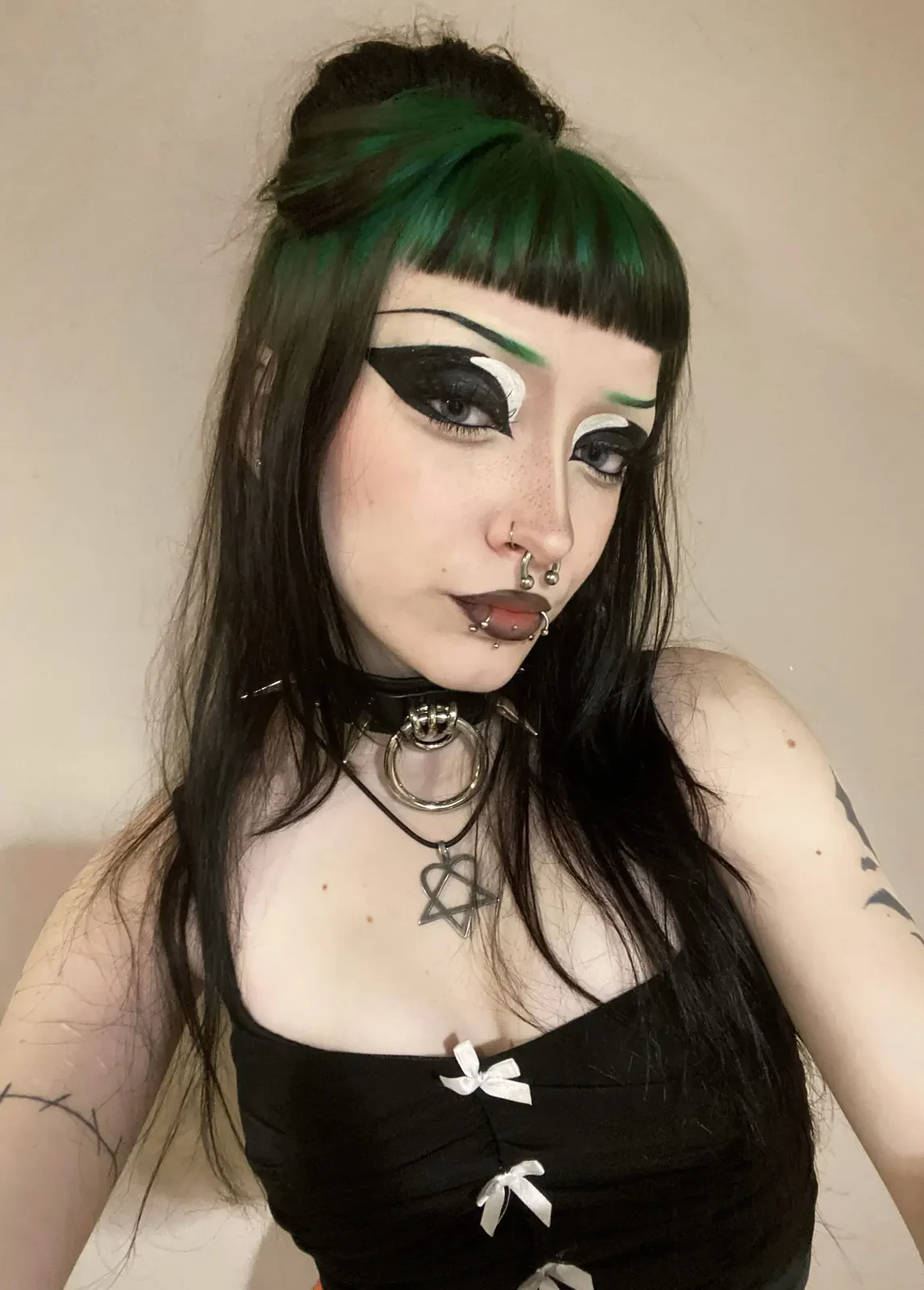 Woman with long straight black hair, a top bun, and a blunt fringe streaked with forest green.