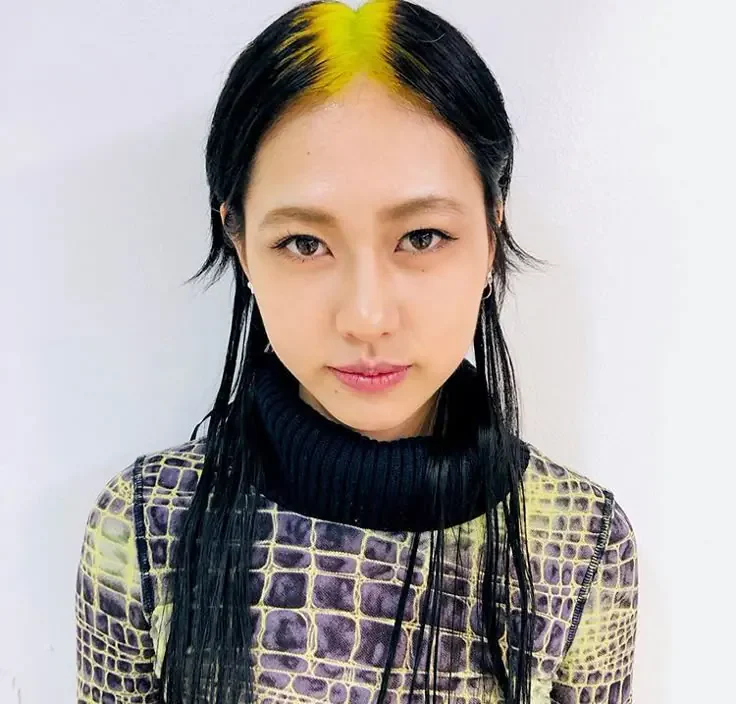 Front portrait of long straight black hair with a narrow neon-yellow root stripe following the center part.