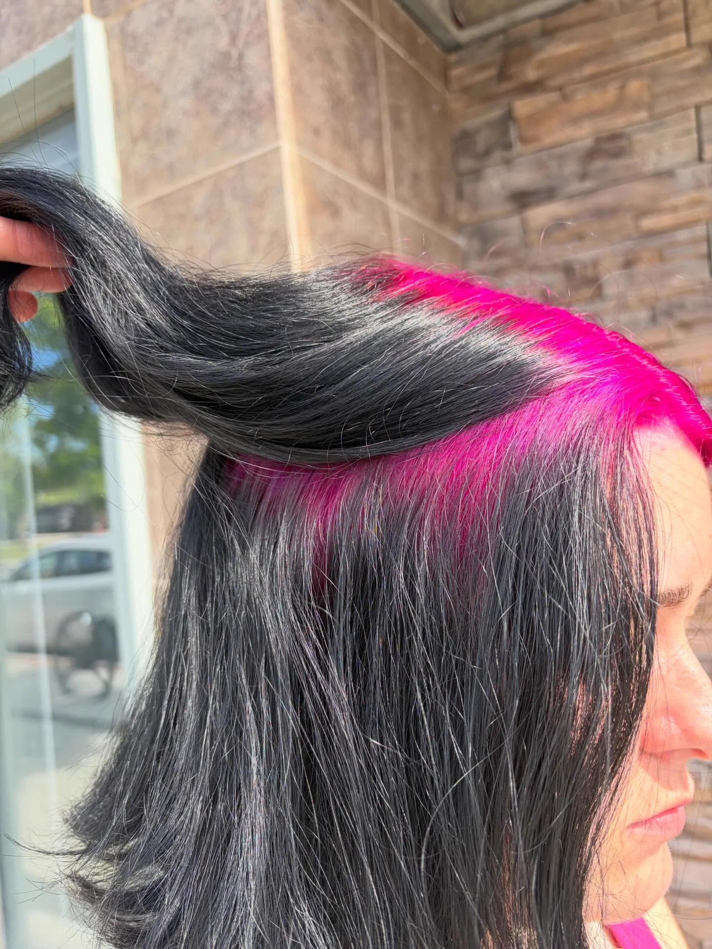 Straight black hair lifted to expose a broad hot-pink side root panel extending from the temple toward the crown.