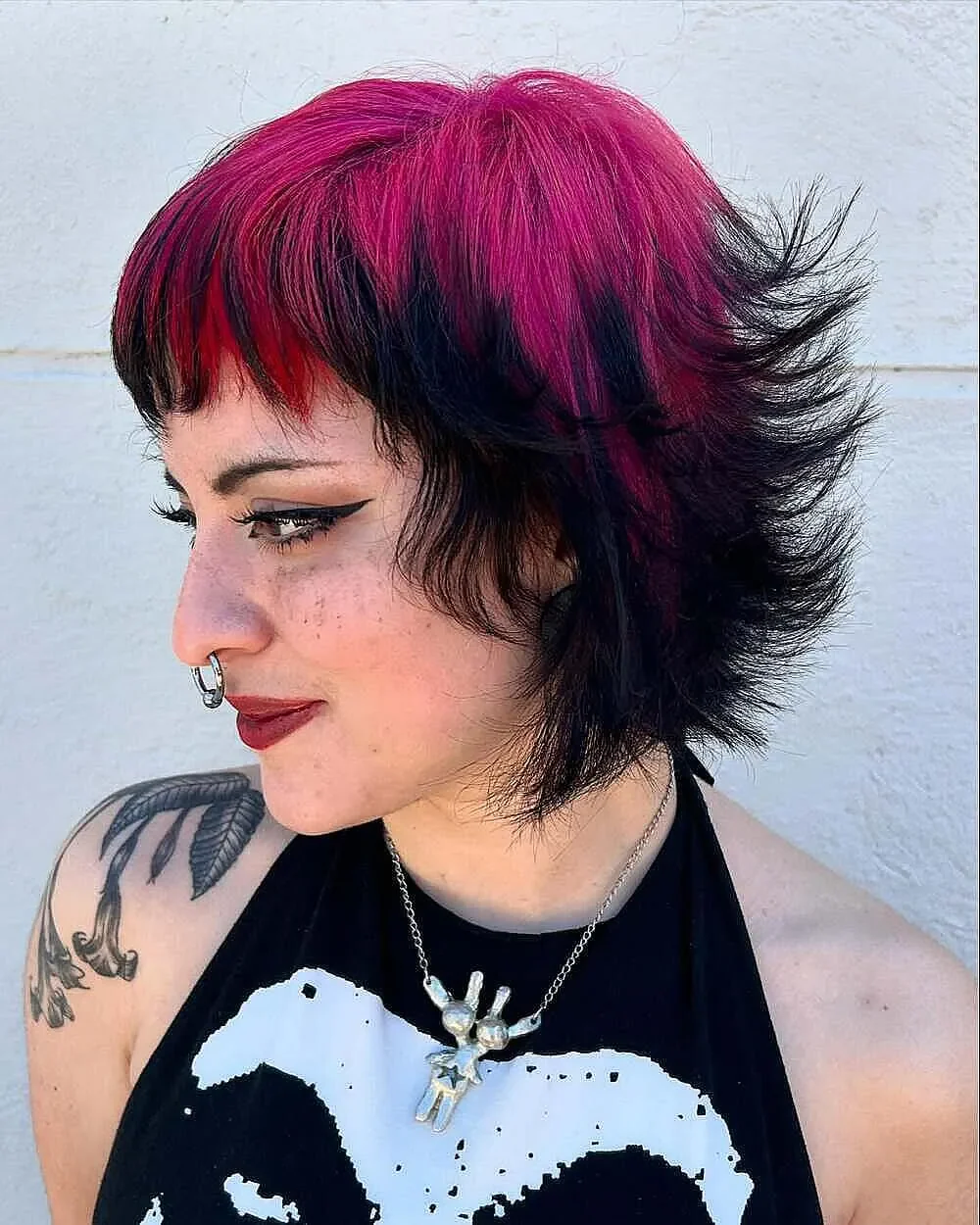 Side portrait of a woman with a short black spiky mullet and pink crown roots.