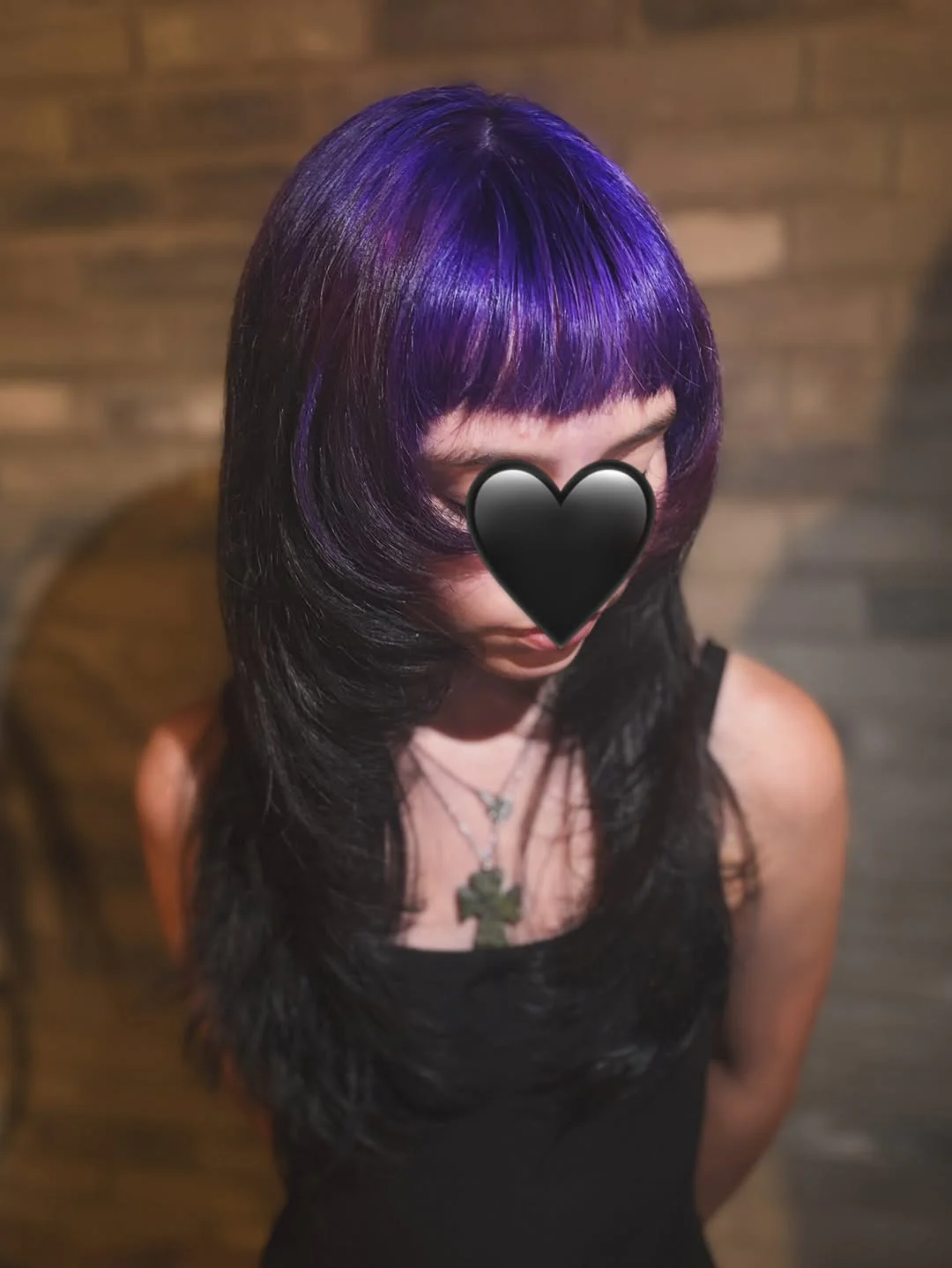 Woman with long black straight layers, a blunt fringe, and violet-purple color across the top roots and bangs.