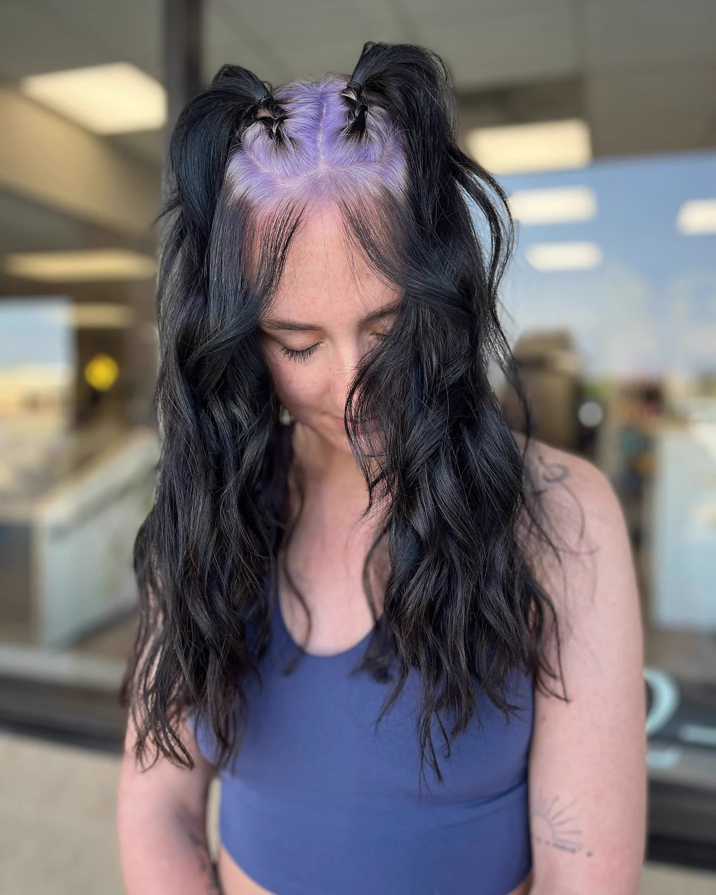 Top-down view of long black wavy hair with purple root sections paired around the center part.