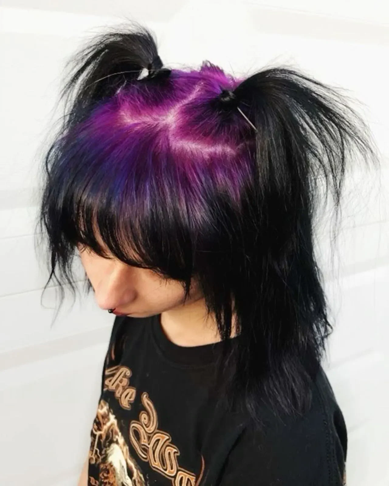 Top view of a woman with medium black hair, blunt bangs, pigtails, and vivid purple crown roots.