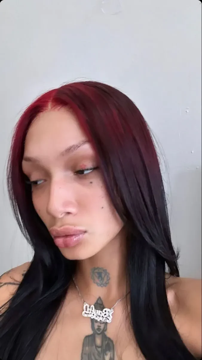 Woman with long sleek black hair and burgundy-red color beginning along the center part.