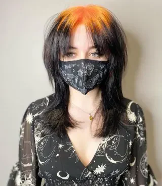 Black wolf cut with orange ghost roots through a split fringe and crown panel.