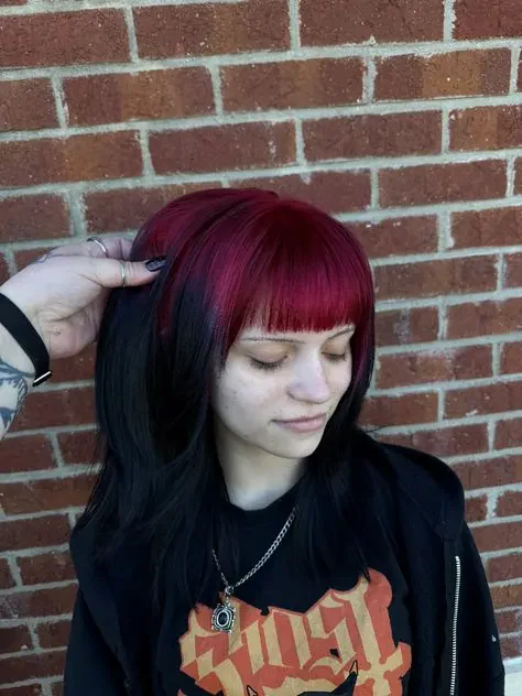 Woman with medium black waves, a full fringe, and burgundy-red color through the fringe roots and top section.