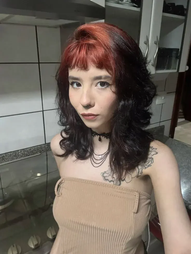Woman with a medium black wavy shag and muted copper-red color across the crown roots and micro fringe.