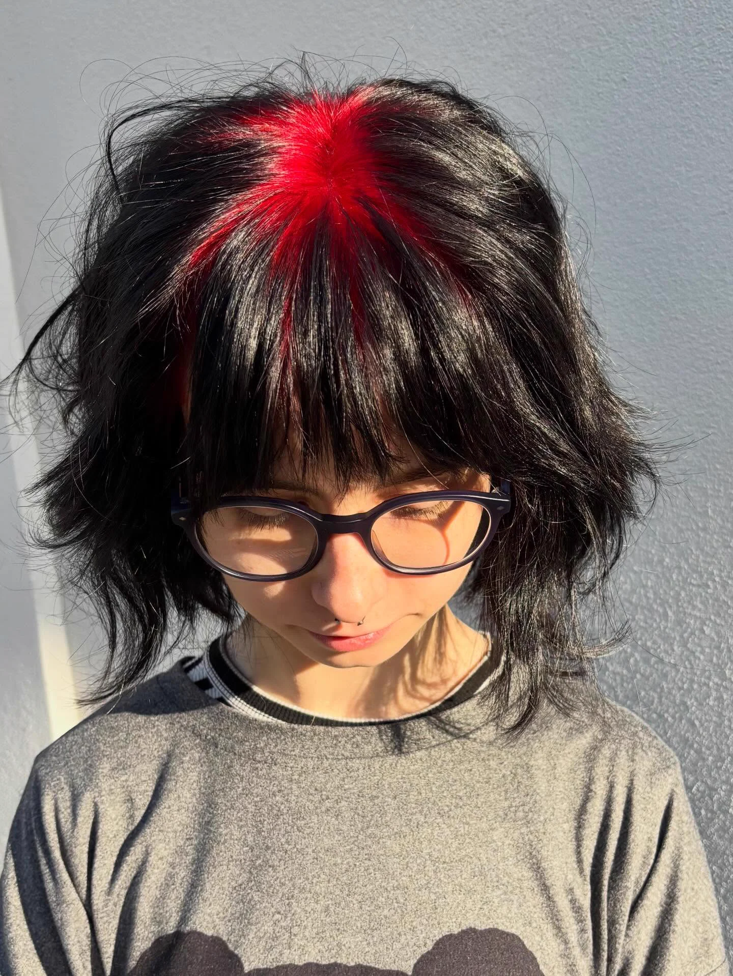 Front top-down view of medium black wavy hair with vivid crimson-red roots through the center crown and fringe.