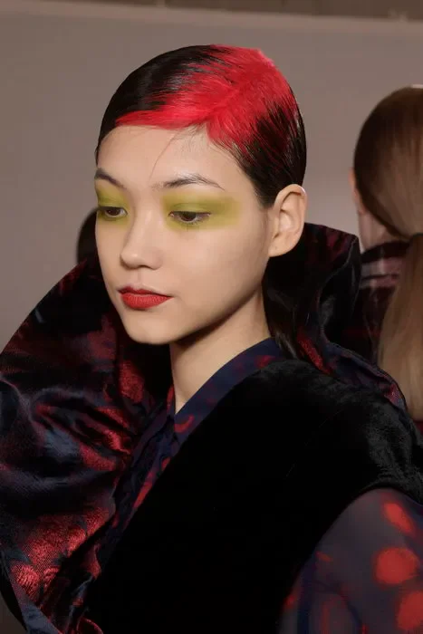 Woman with short slicked-back black hair and a broad vivid-red wash across the exposed root zone.
