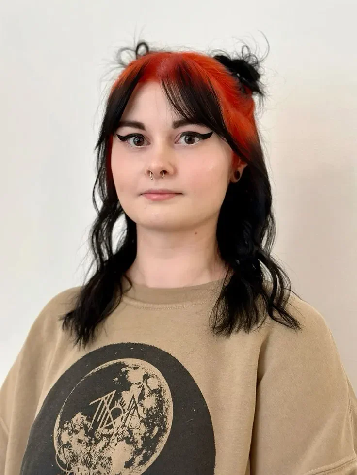 Woman with short black hair, two small buns, and vivid crimson-red sections beginning on both sides of the center part.
