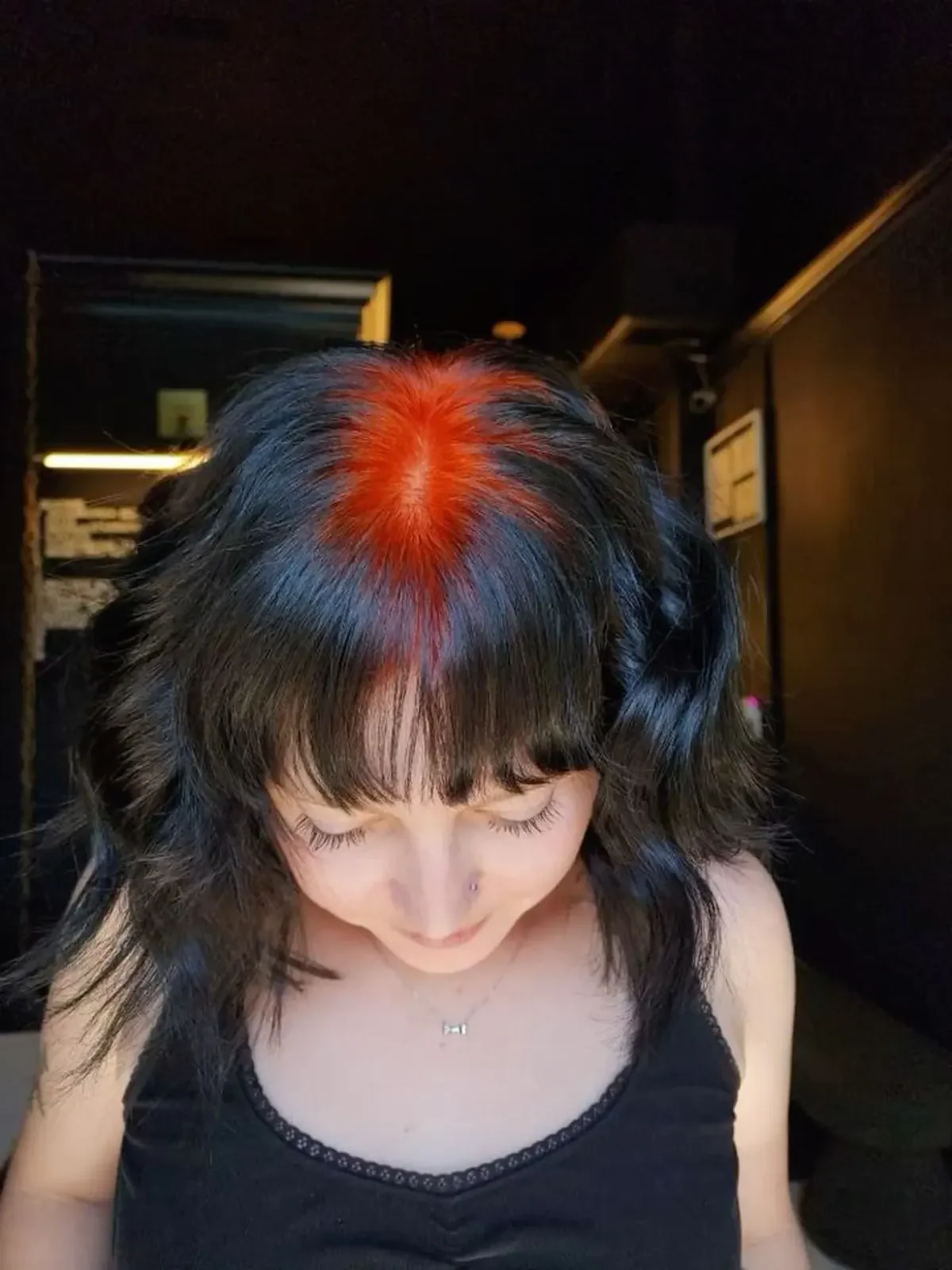 Top view of a woman with short black hair in pigtails and vivid red-orange color across the center-part and crown roots.