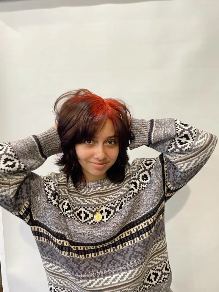 Woman with a short black wavy bob and orange-copper color concentrated through the top crown roots.