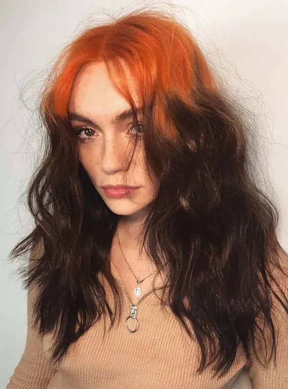 Woman with long dark brown waves and copper-orange sections beginning at both sides of the center part and split fringe.