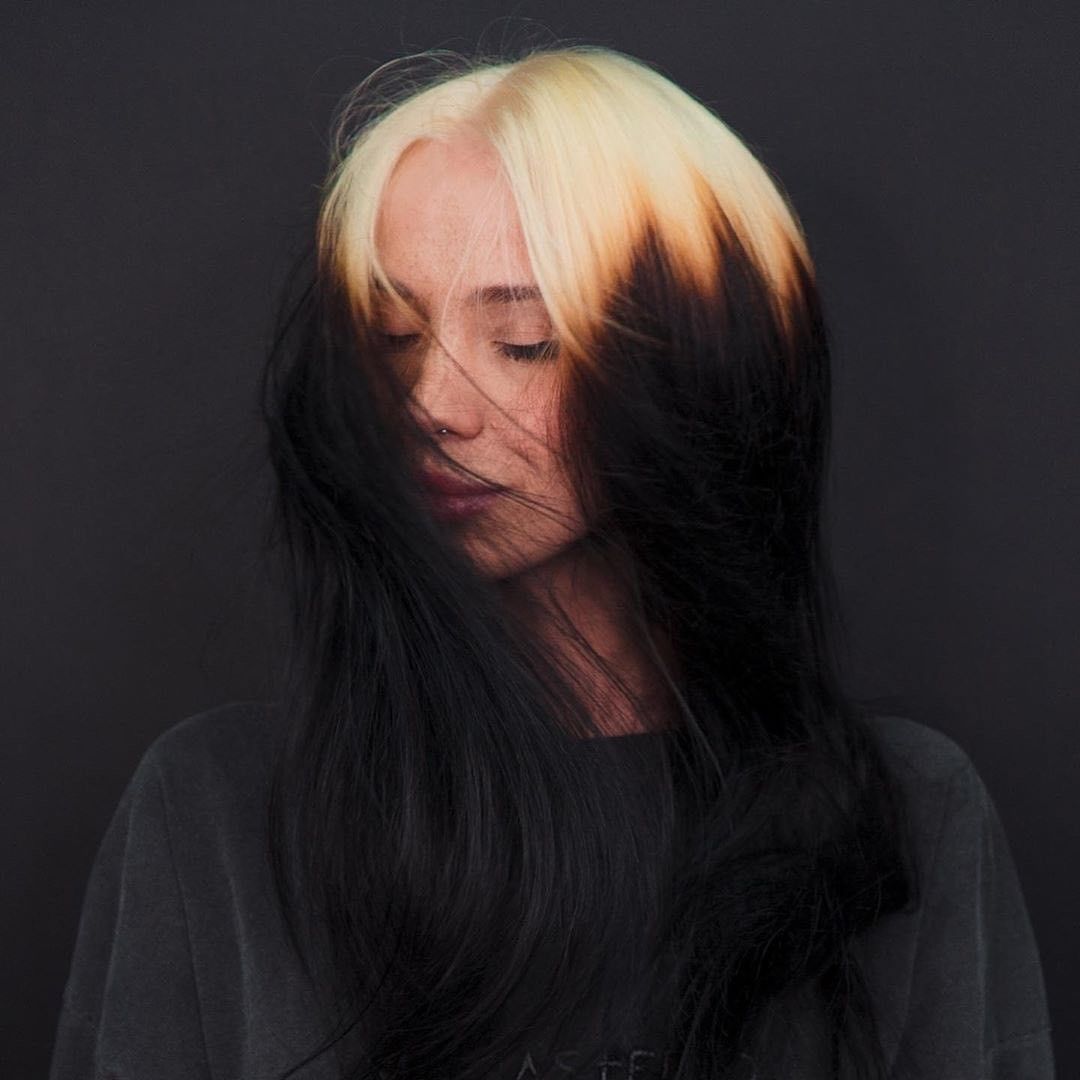 Long black hair with creamy blonde ghost roots and soft face-framing layers.