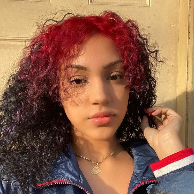 Long black curly hair with crimson red ghost roots through the top panel.