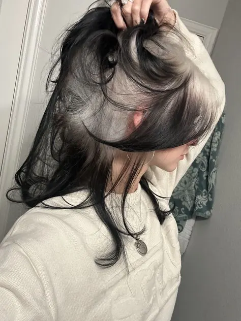 Dark hair lifted to reveal a hidden silver blonde ghost-roots underlayer.