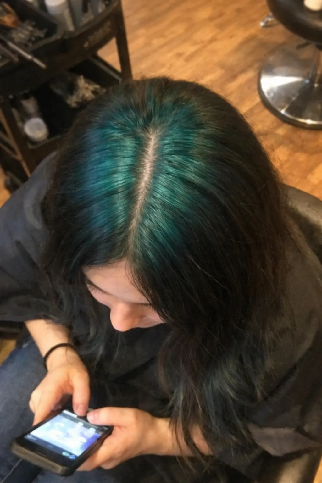 Medium-long black hair with teal ghost roots visible along the center part and crown.