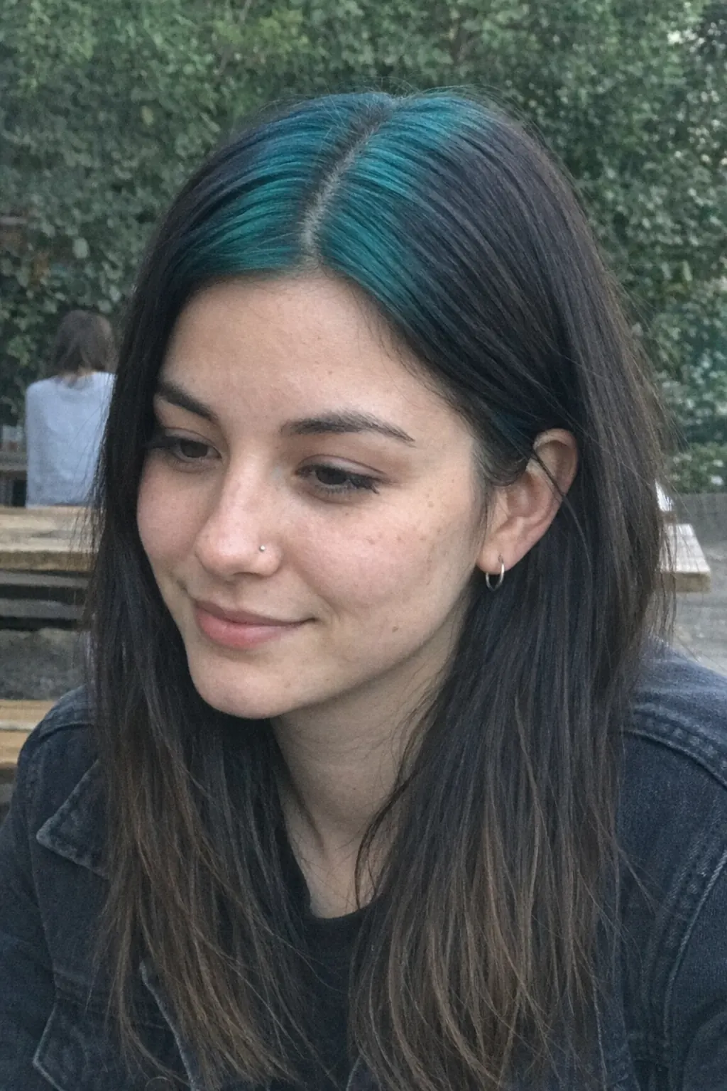 Medium-long black straight layered hair with teal ghost roots along the center part.