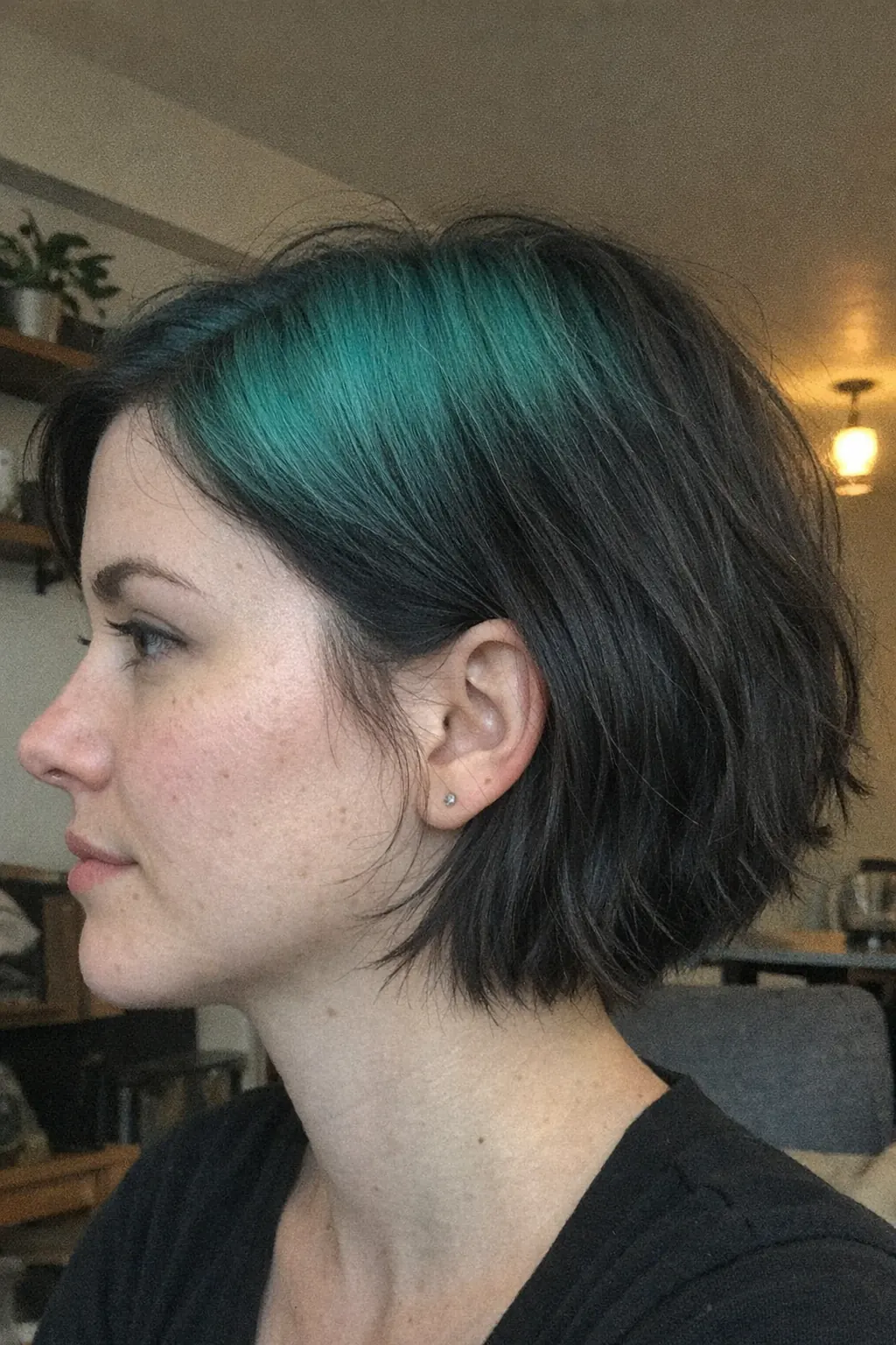 Short black French bob with teal ghost roots through the side part.