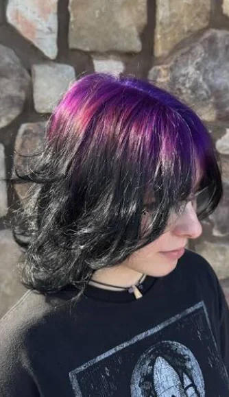 Side view of a short layered black bob with a vivid violet-magenta crown panel.
