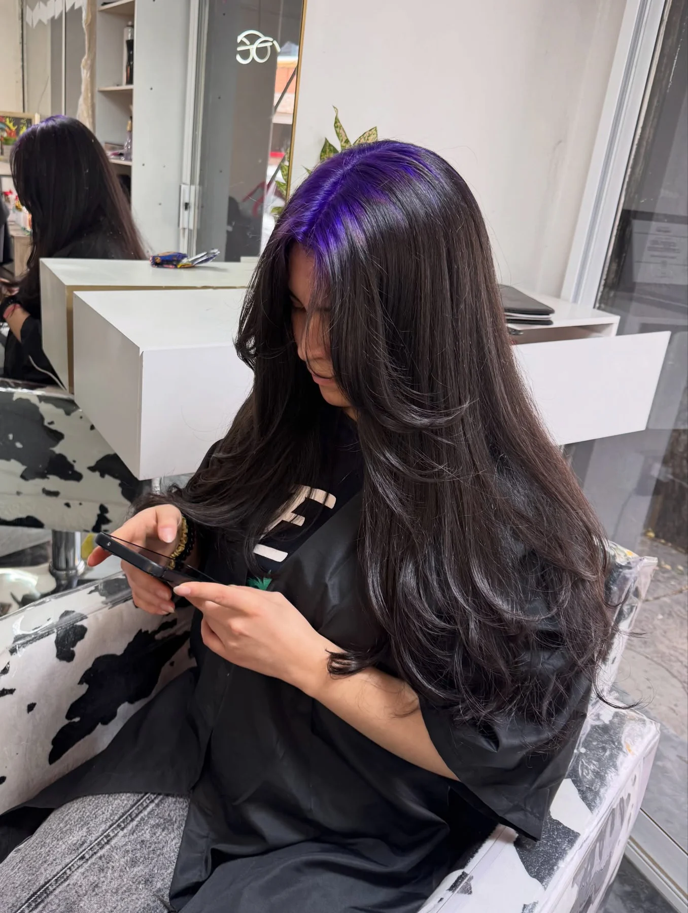 Woman with a very long black layered blowout and vivid-violet roots concentrated on one side of the part.