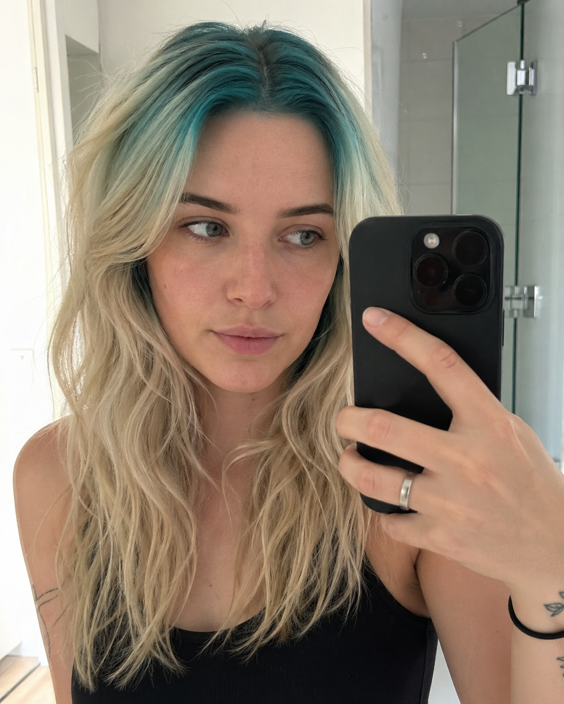 Long blonde loose waves with teal-blue ghost roots through the top root panel.
