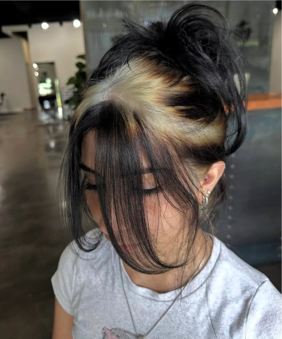 Medium black hair in a messy updo with silver-blonde ghost roots and face-framing bangs.