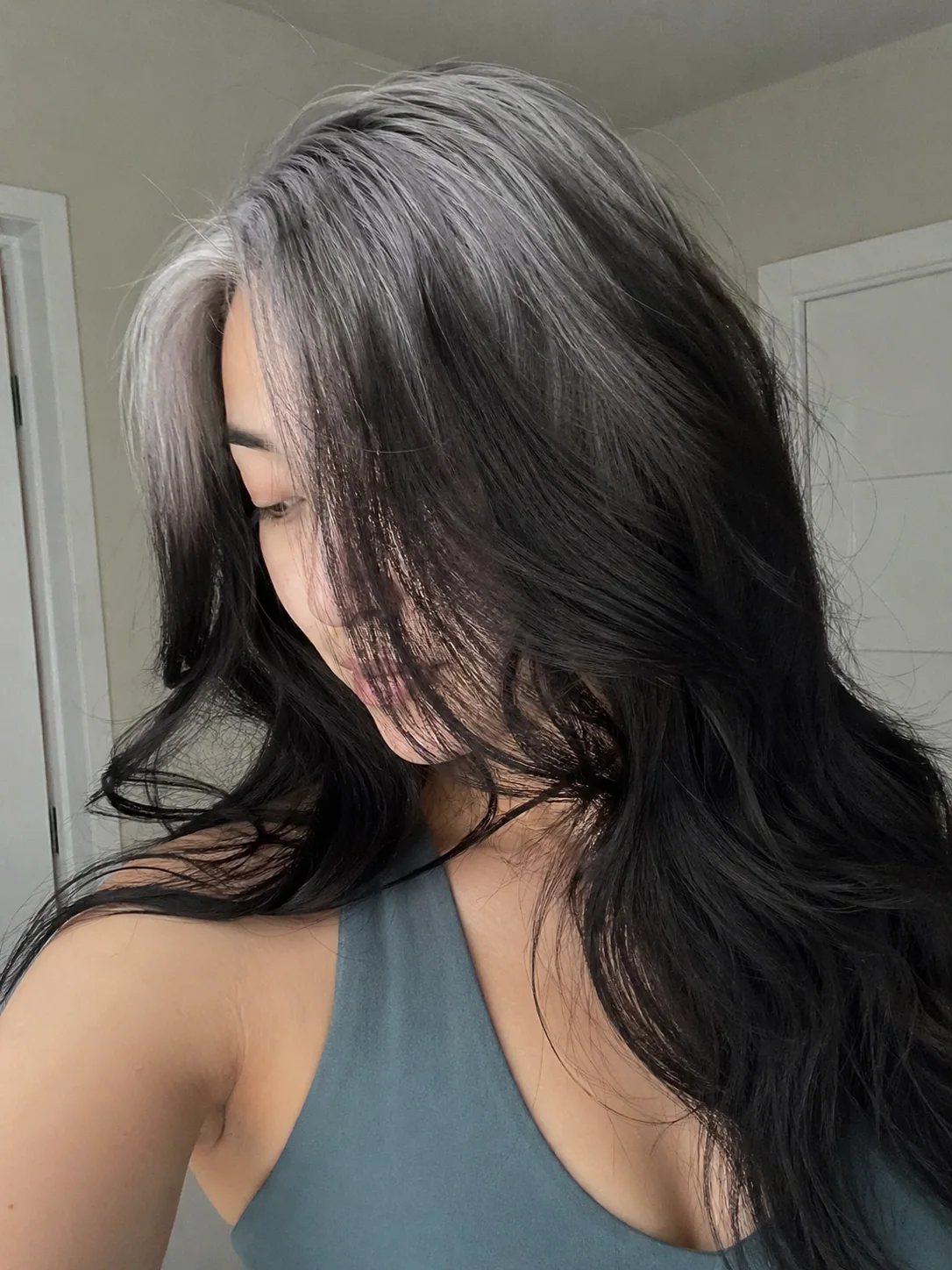 Long black layered waves with smoky silver ghost roots through a side-swept part.
